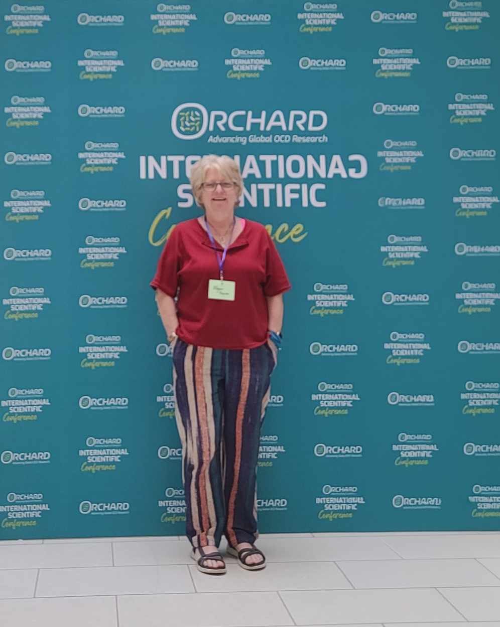 Megan Karnes standing behind the Orchard International Scientific conference background in June 2026